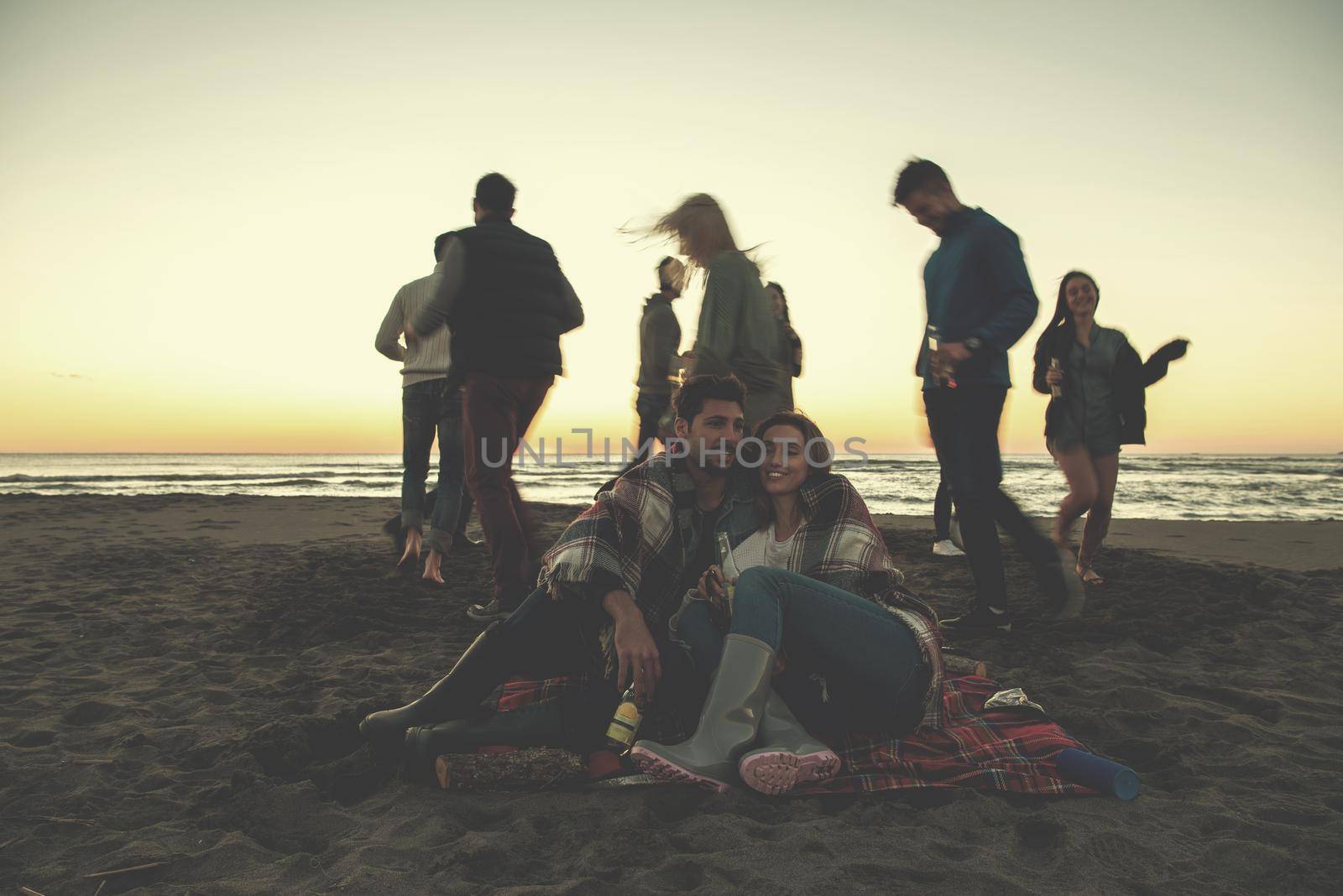 Young Couple enjoying with friends Around Campfire on The Beach At sunset drinking beer