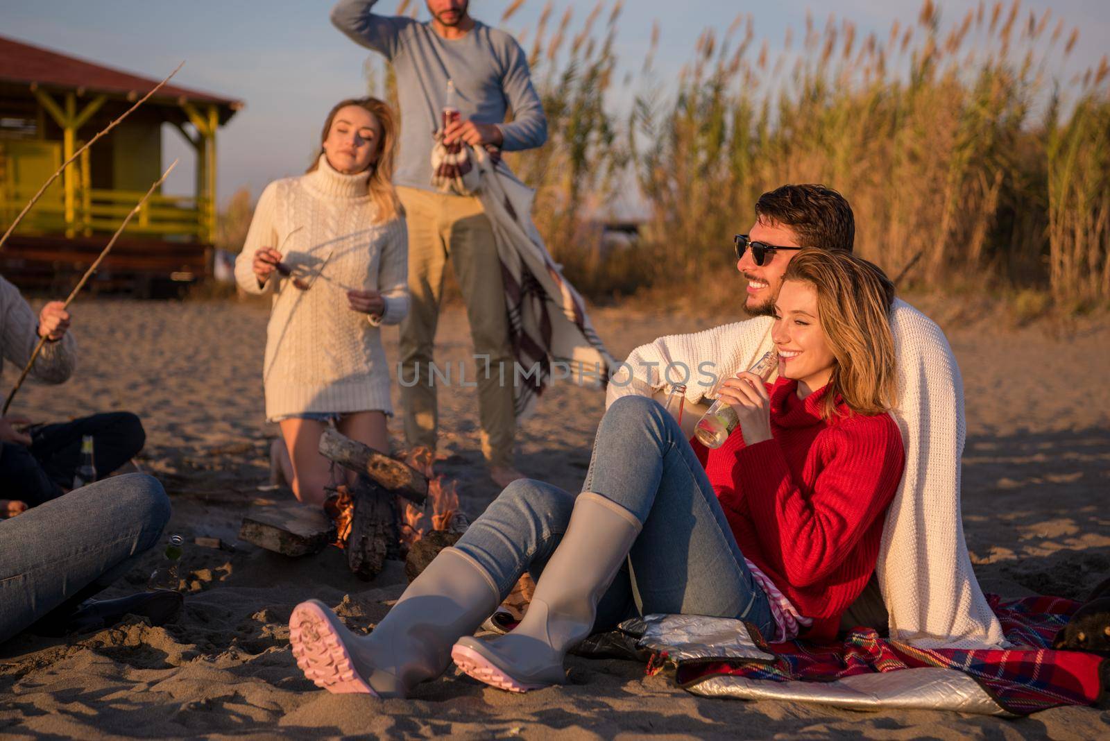 Young Couple enjoying with friends Around Campfire on The Beach At sunset drinking beer