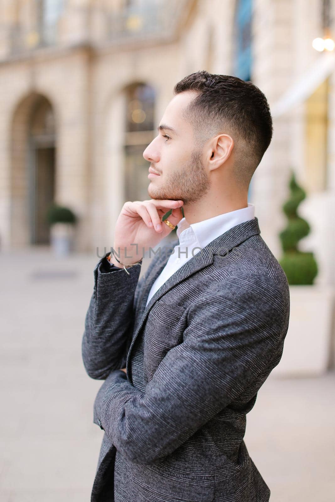 Young caucasian boy wearing grey suit standing near building. Concept of male fashion and successful businessman.