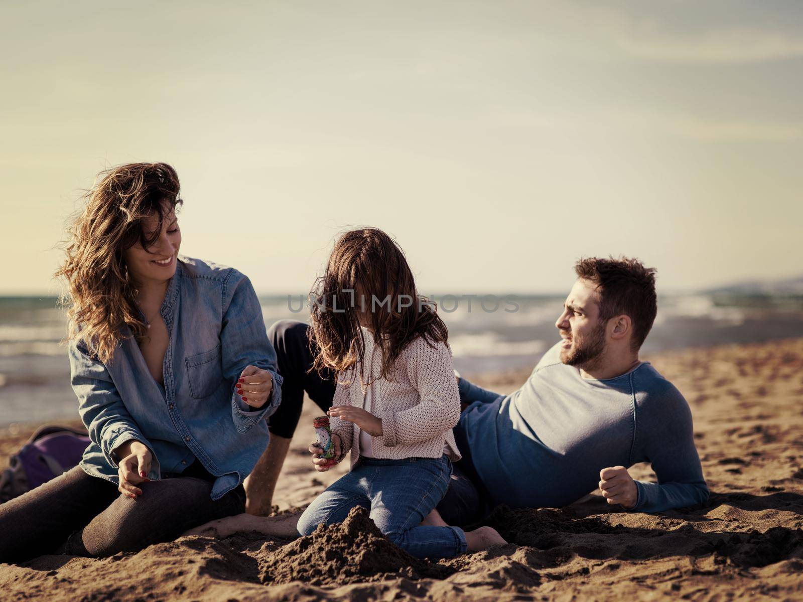 Family with little daughter resting and having fun at beach during autumn day colored filter