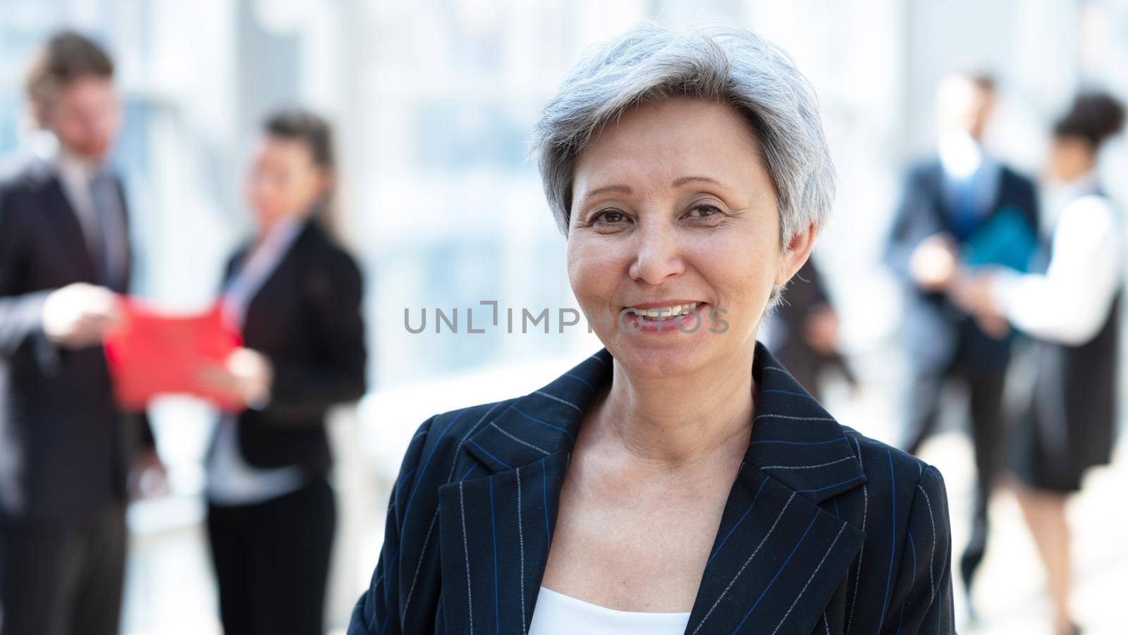 Happy successful mature Asian businesswoman posing in front of colleagues in business building