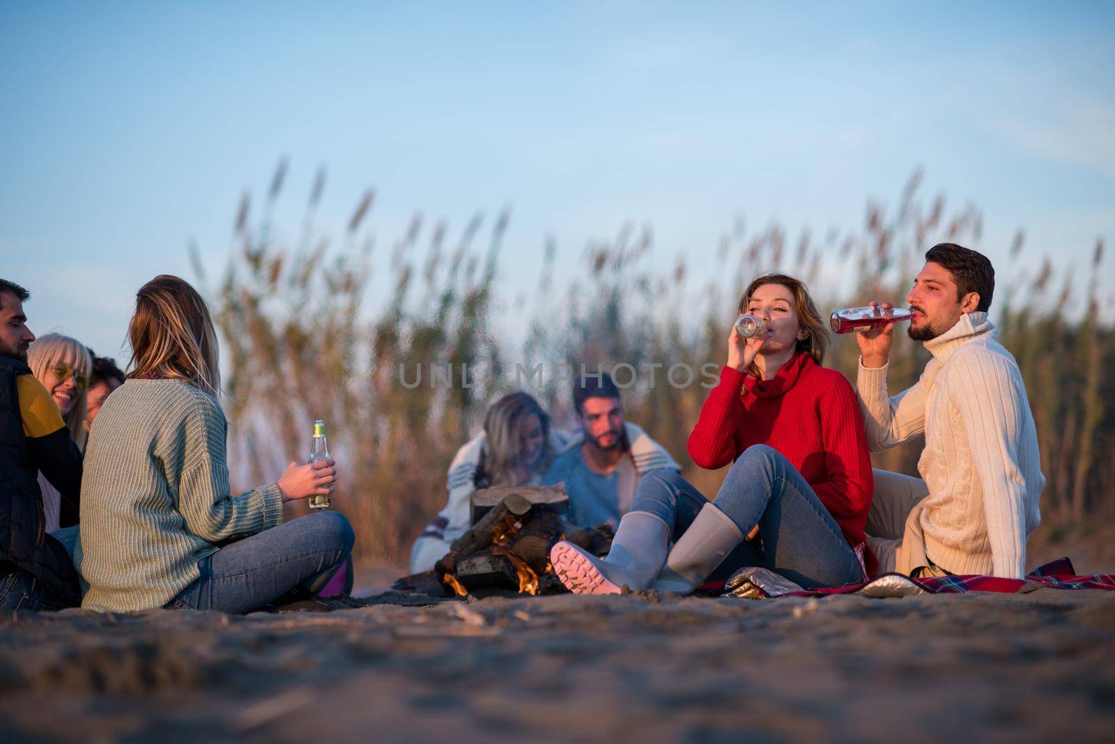 Young Couple enjoying with friends Around Campfire on The Beach At sunset drinking beer