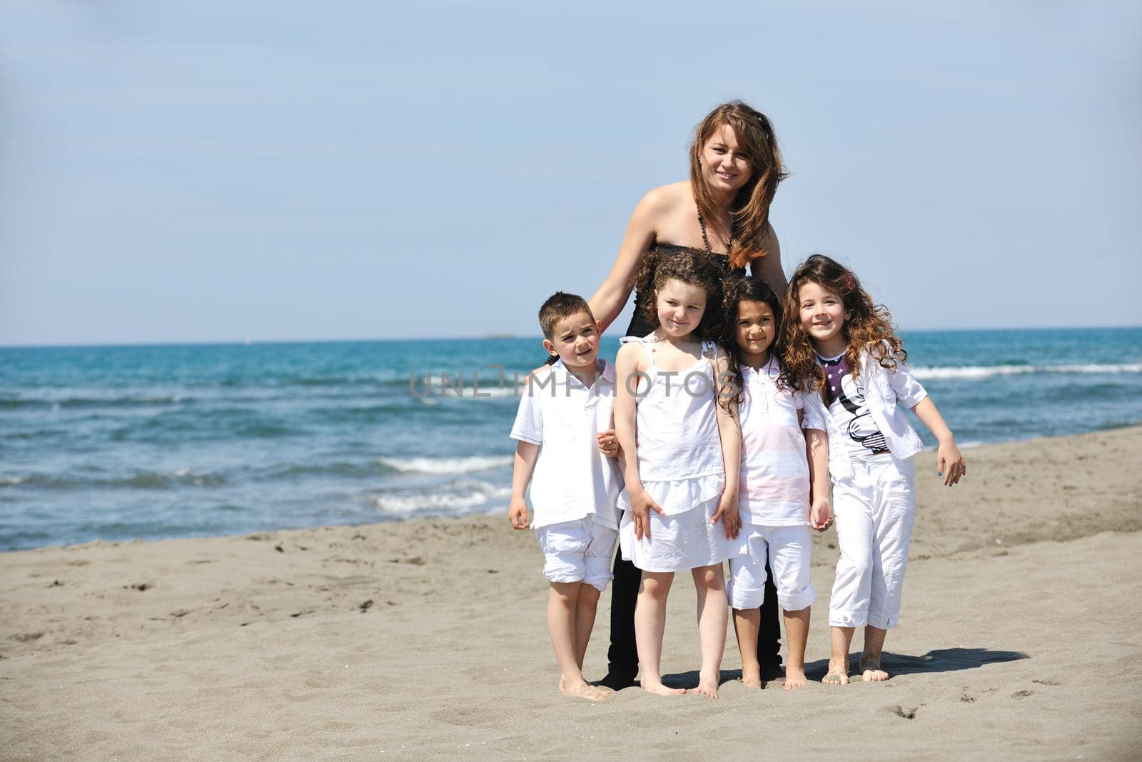 group portrait of happy childrens with young female  teacher on beach