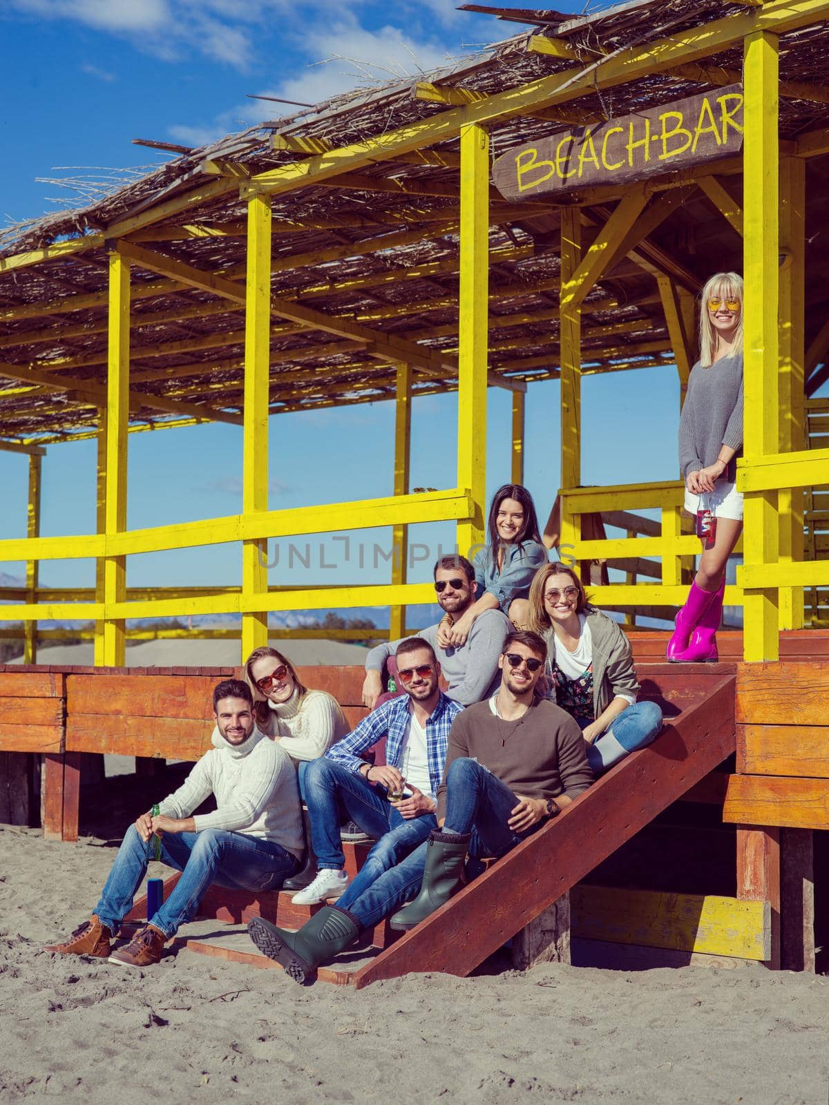 Happy Group Of Friends Hanging Out At Beach House having fun and drinking beer on autumn day colored filter