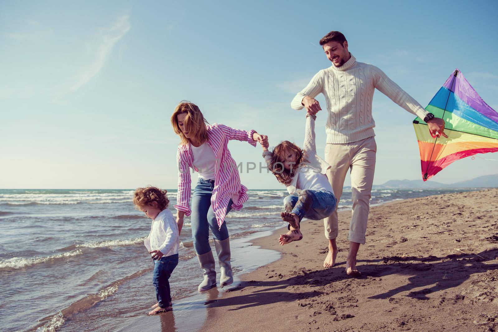 young family with kids resting and having fun with a kite at beach during autumn day filter