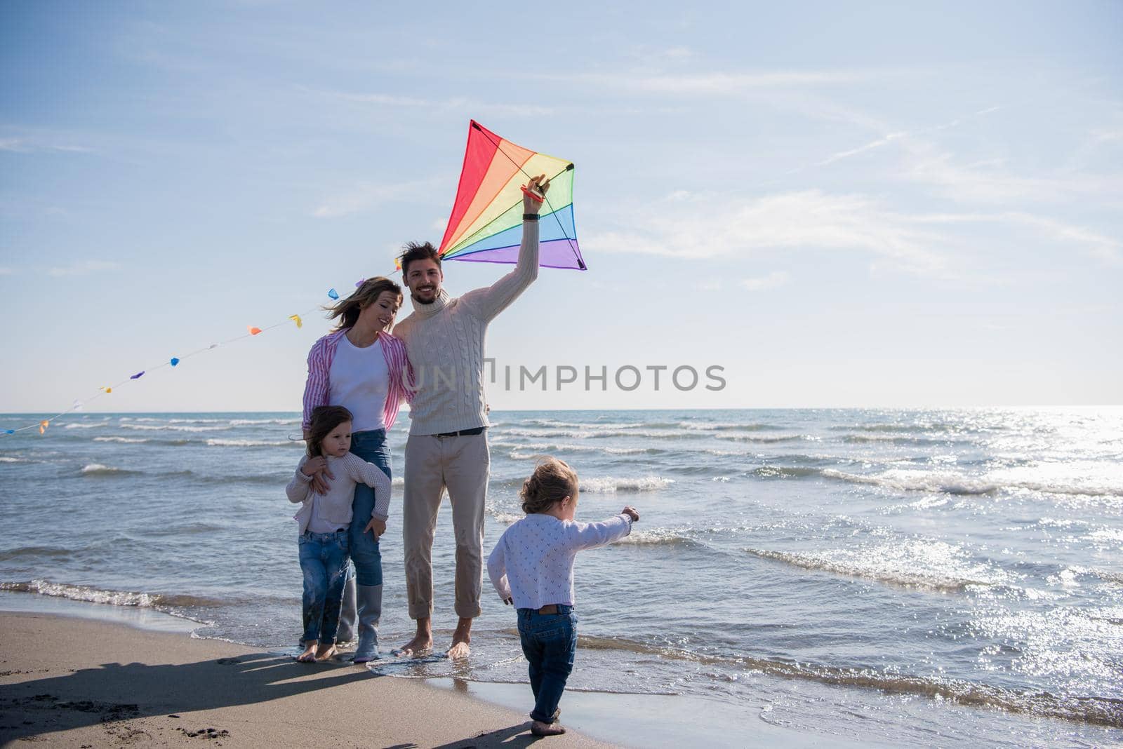 young family with kids resting and having fun with a kite at beach during autumn day