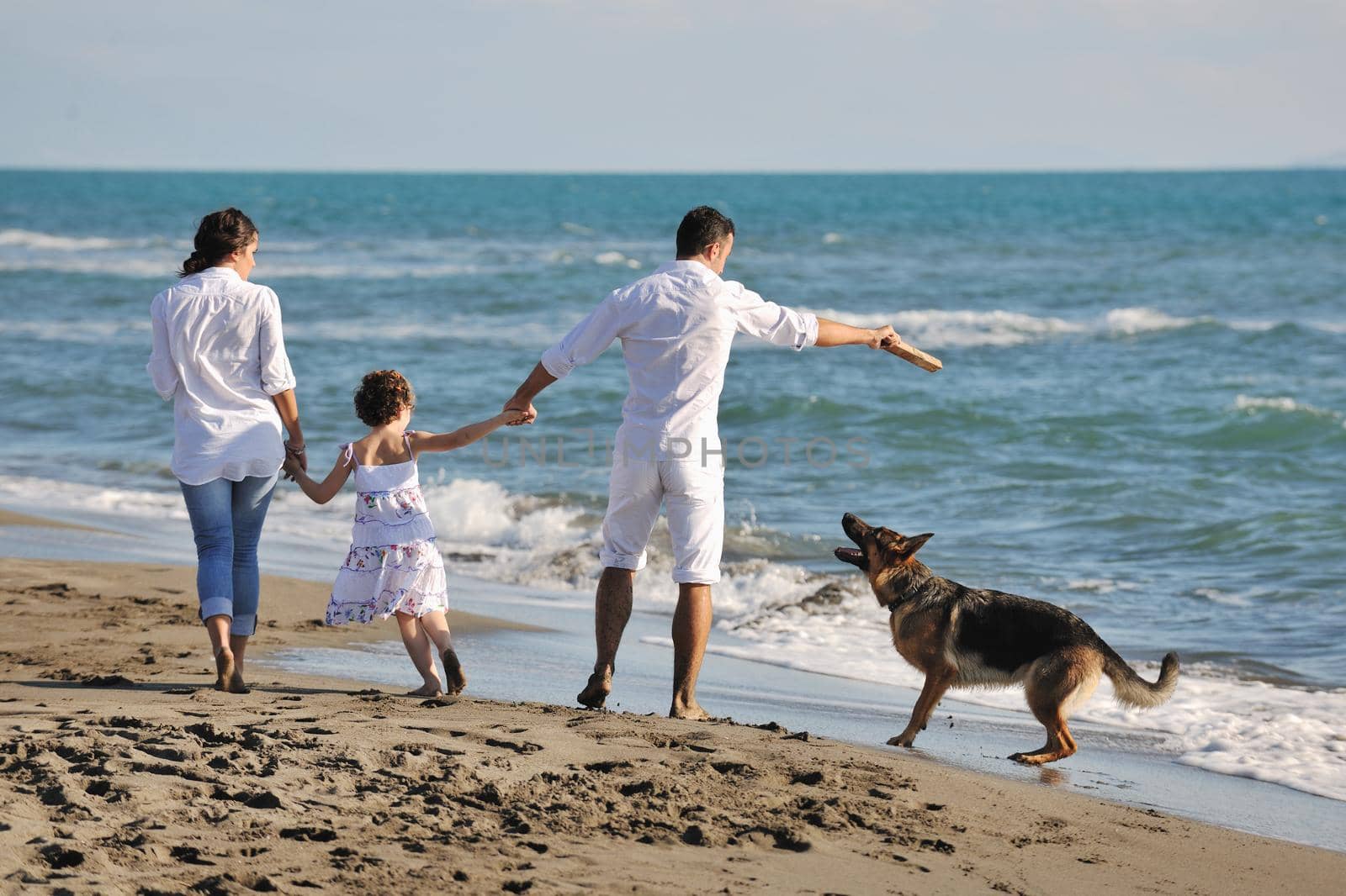 happy young family in white clothing have fun and play with beautiful dog at vacations on beautiful beach 