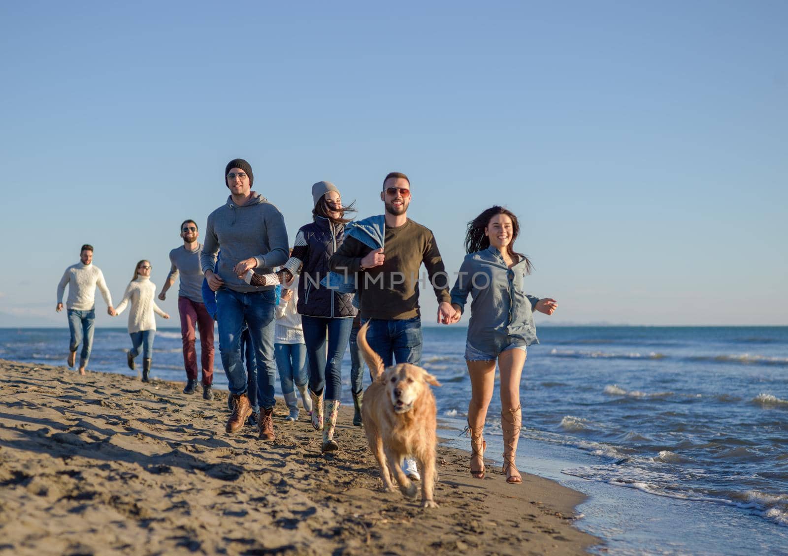 Group of friends running on beach during autumn day by dotshock