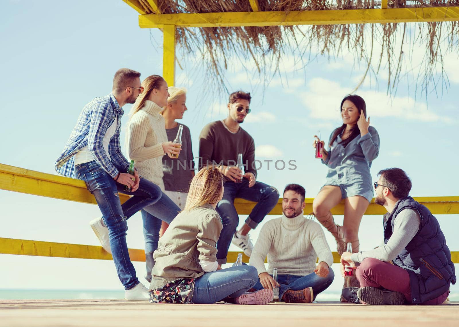 Happy Group Of Friends Hanging Out At Beach House having fun and drinking beer on autumn day colored filter