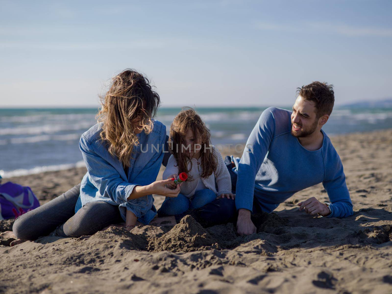 Family with little daughter resting and having fun at beach during autumn day colored filter