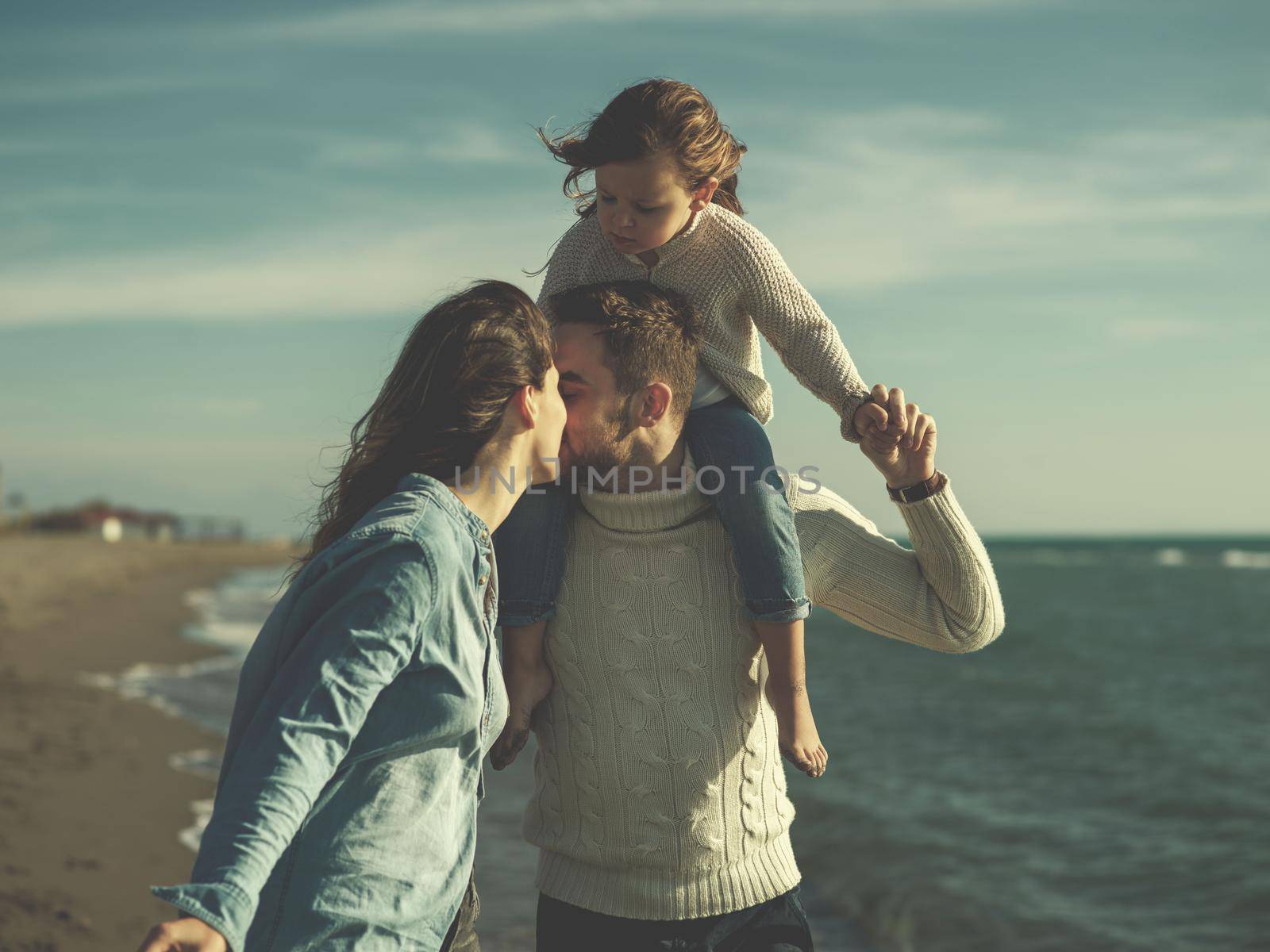 Family with little daughter resting and having fun at beach during autumn day colored filter