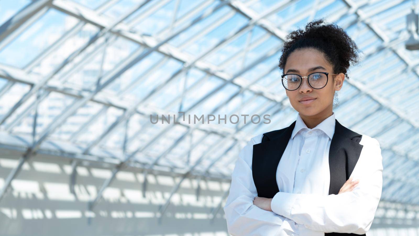 Close up portrait of young mixed race business woman standing with arms crossed in modern office