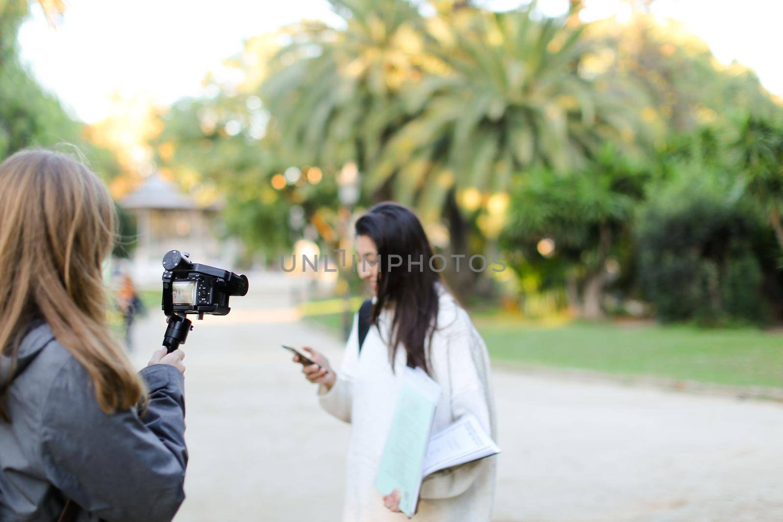 Focus on photographer taking photo of blurred chinese gril with smartphone and papers. Concept of photosession in open air, camera.