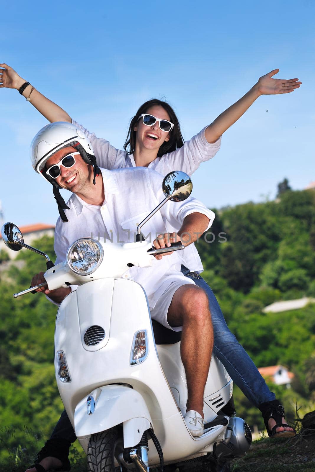 Portrait of happy young love couple on scooter enjoying themselves in a park at summer time