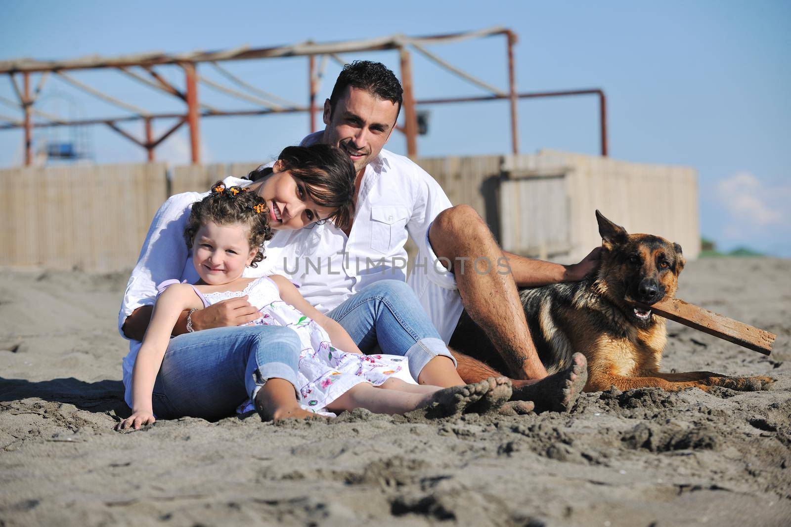 happy young family in white clothing have fun and play with beautiful dog at vacations on beautiful beach 