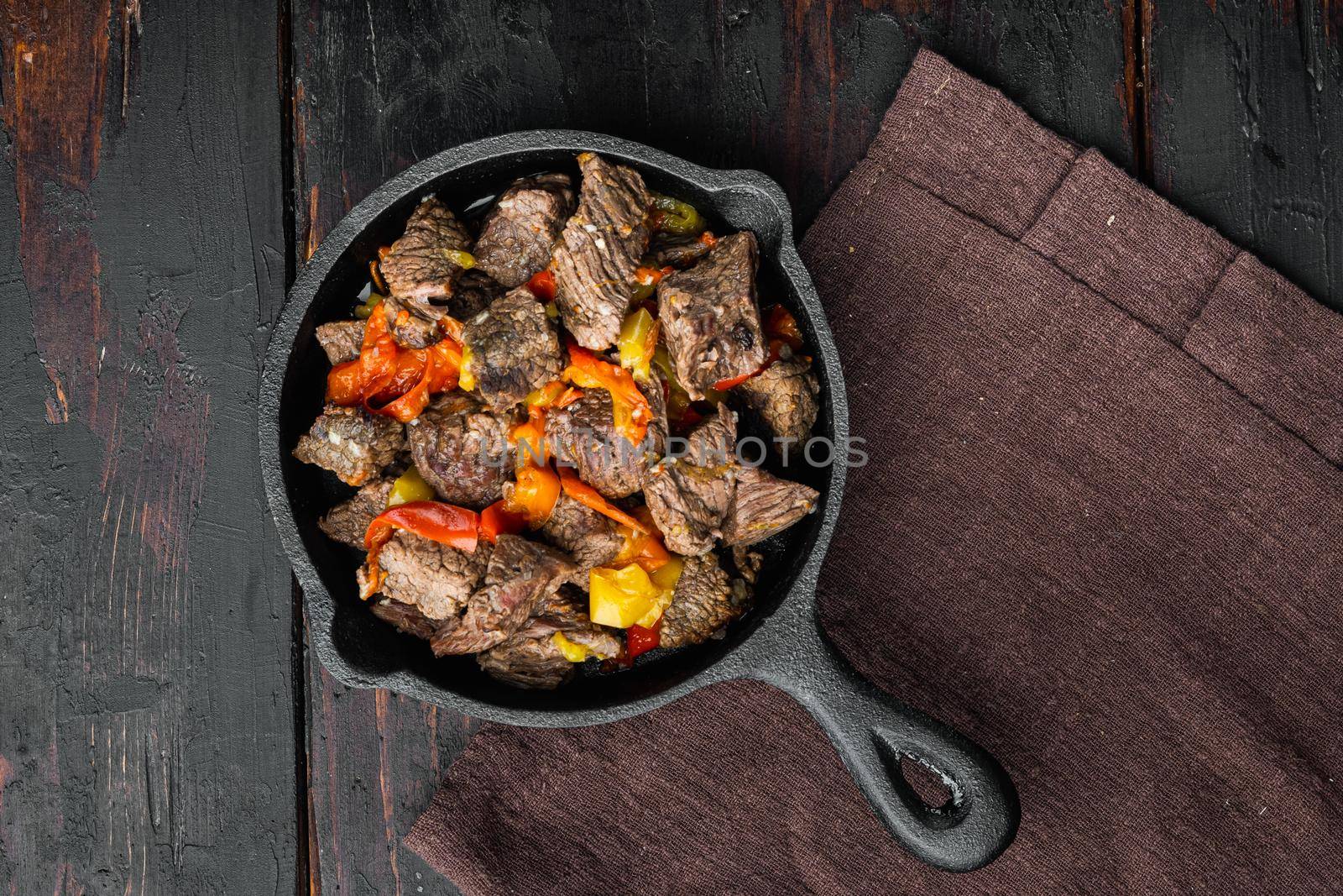 Beef meat stewed with potatoes, carrots and spices set, in cast iron frying pan, on old dark wooden table, top view flat lay, with copy space for text