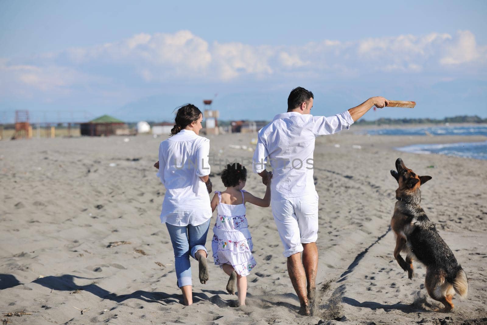 happy young family in white clothing have fun and play with beautiful dog at vacations on beautiful beach 