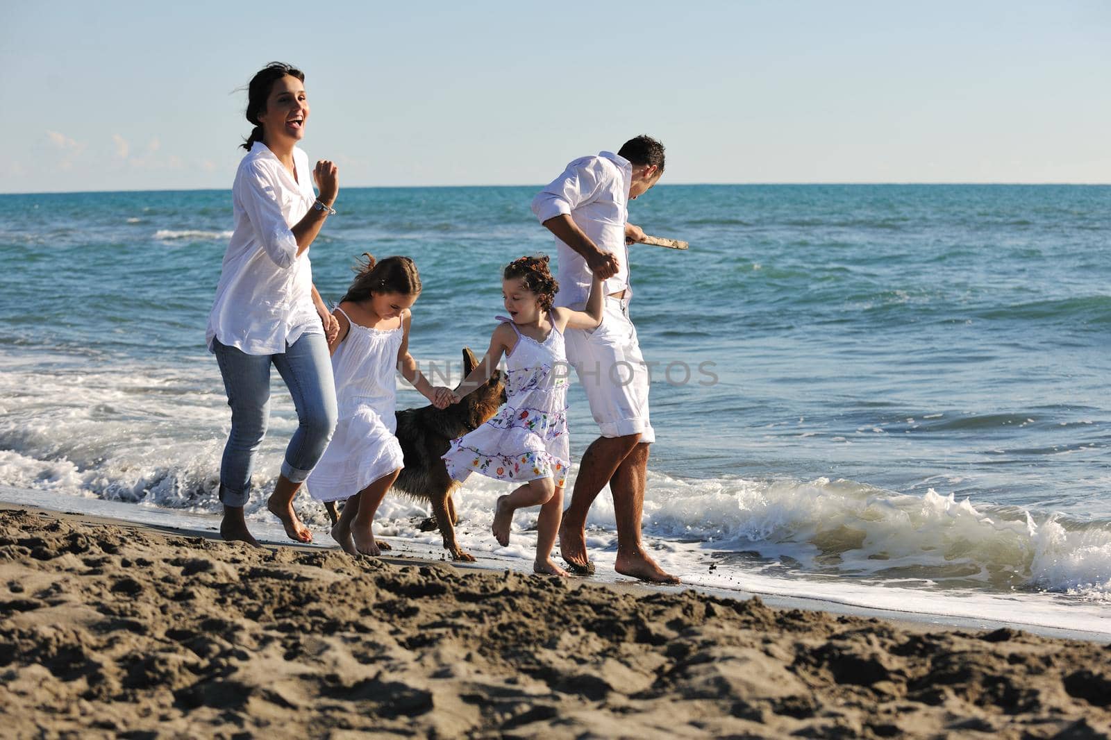 happy young family in white clothing have fun and play with beautiful dog at vacations on beautiful beach 