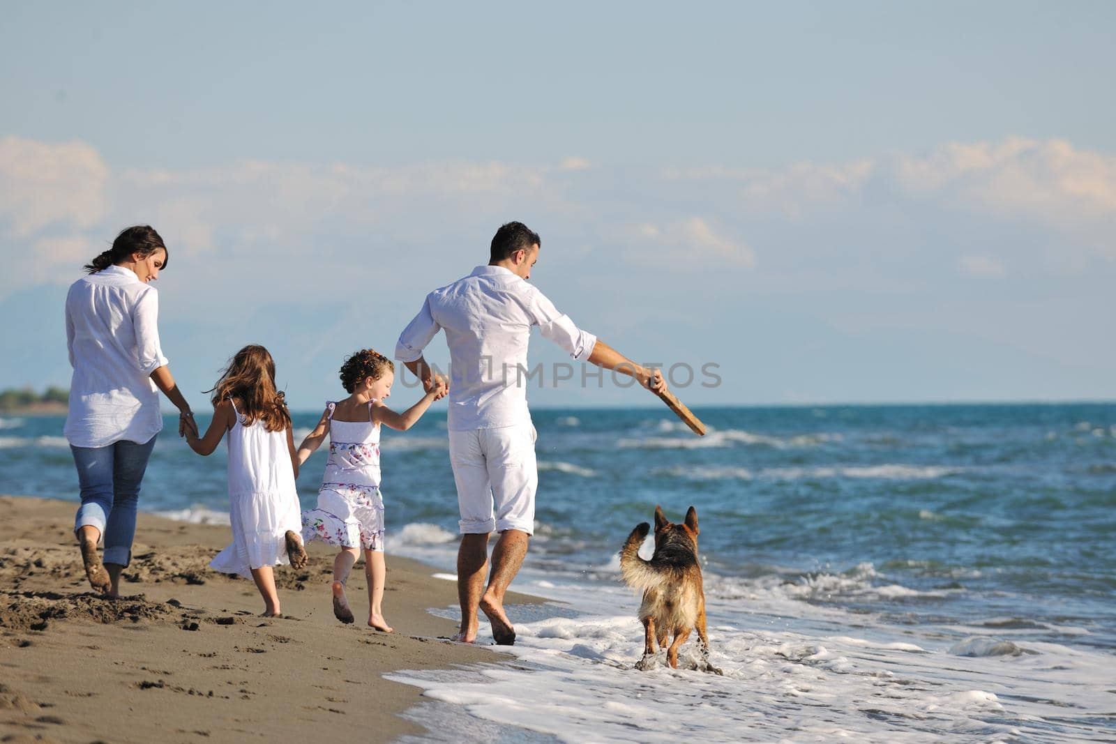 happy young family in white clothing have fun and play with beautiful dog at vacations on beautiful beach 