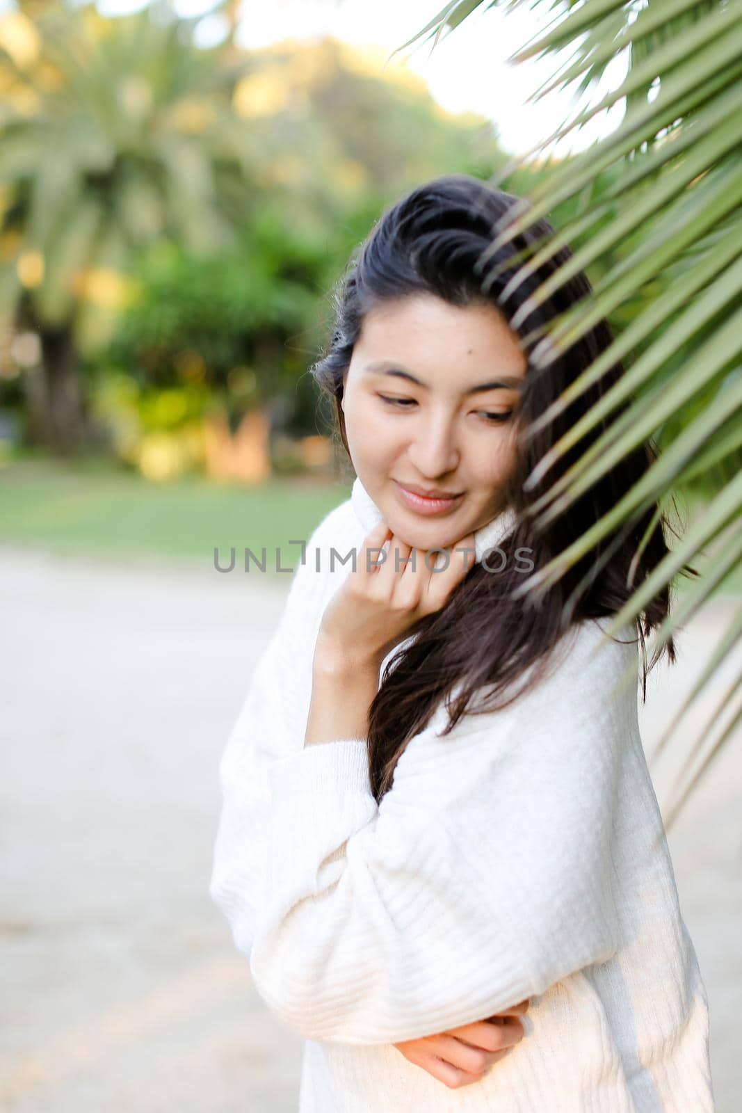 Portrait of chinese woman wearing white sweater standing near palm leaf. Concept of asian beauty and female person.