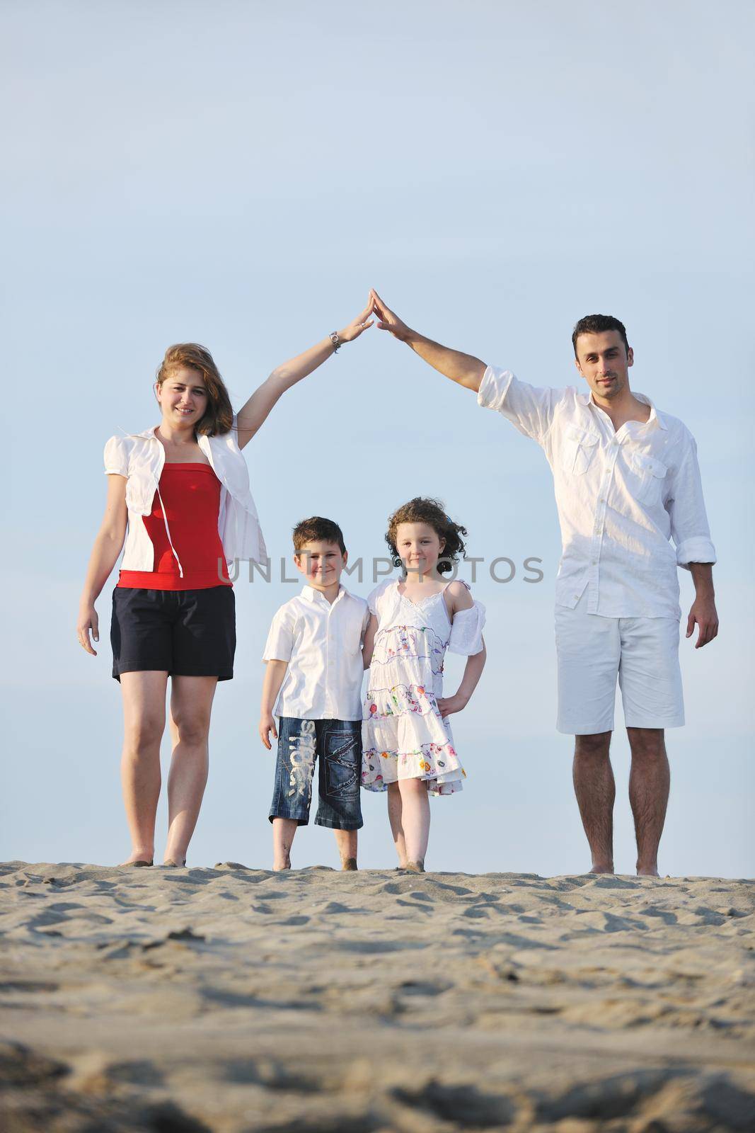 happy young family have fun on beachand showing home sign with conncected hands while protecting childrens