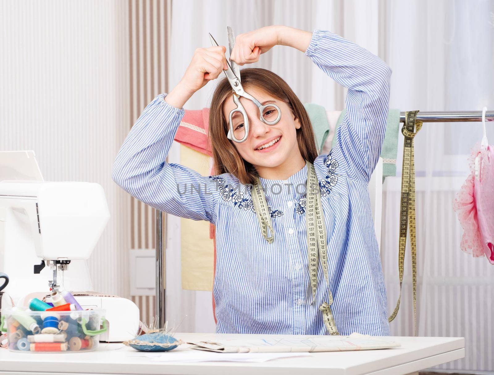 Cute young tailor with scissors at workspace