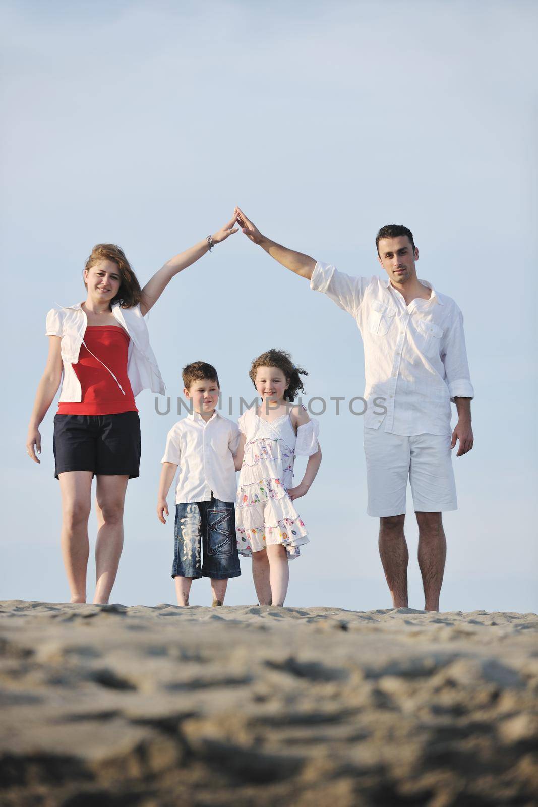 happy young family have fun on beachand showing home sign with conncected hands while protecting childrens