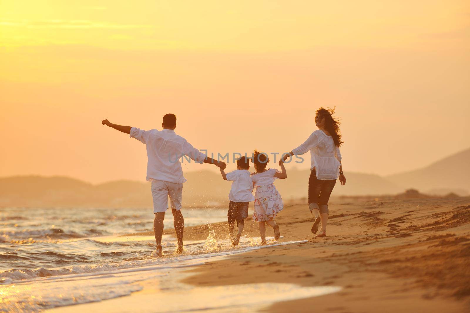 happy young family have fun on beach run and jump  at sunset