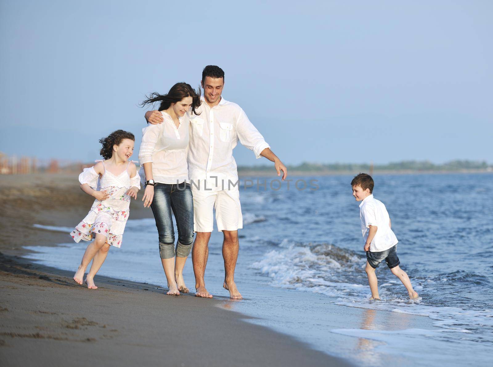 happy young family have fun on beach run and jump  at sunset