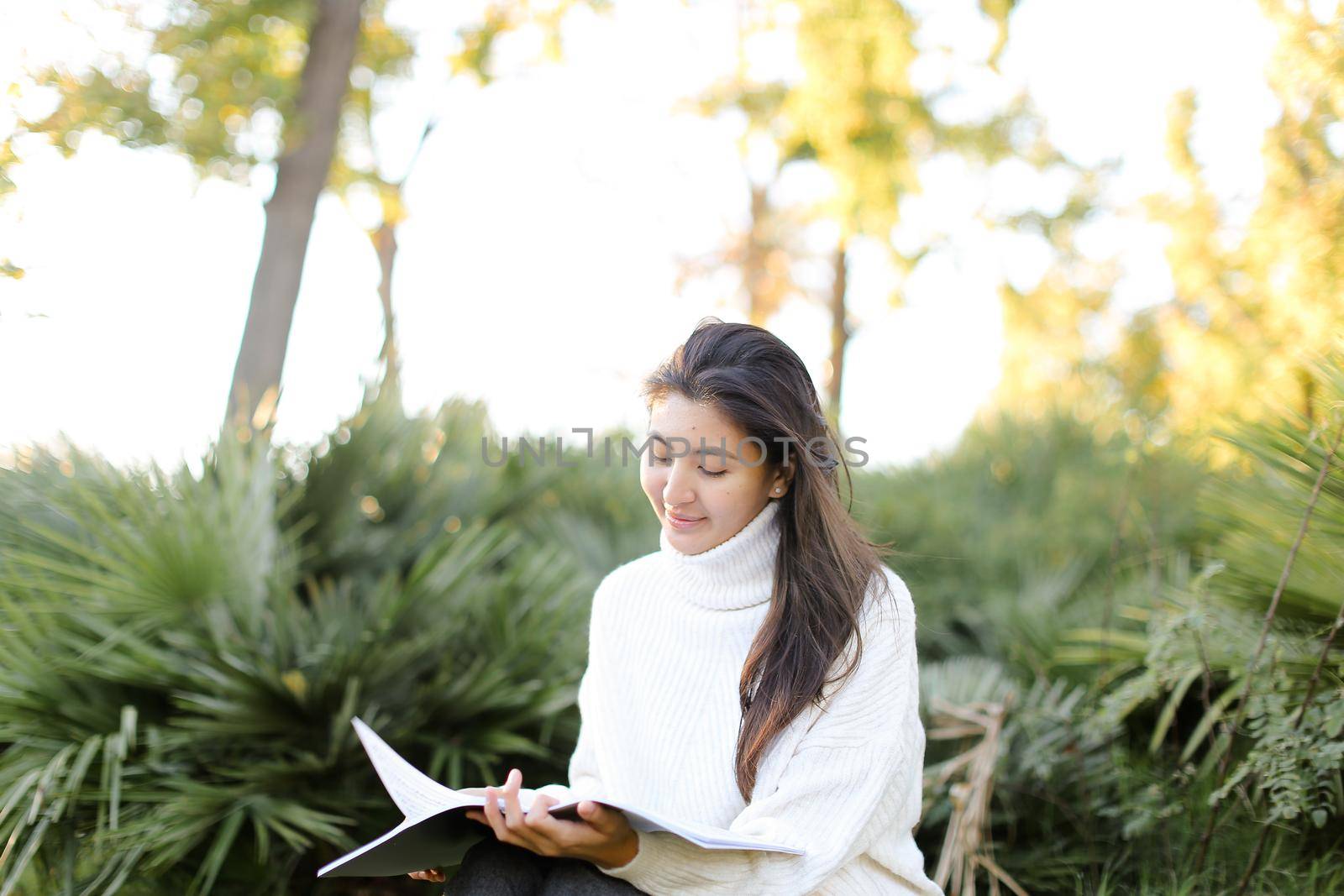 Chinese girl sitting on stump in park and reading papers. by sisterspro