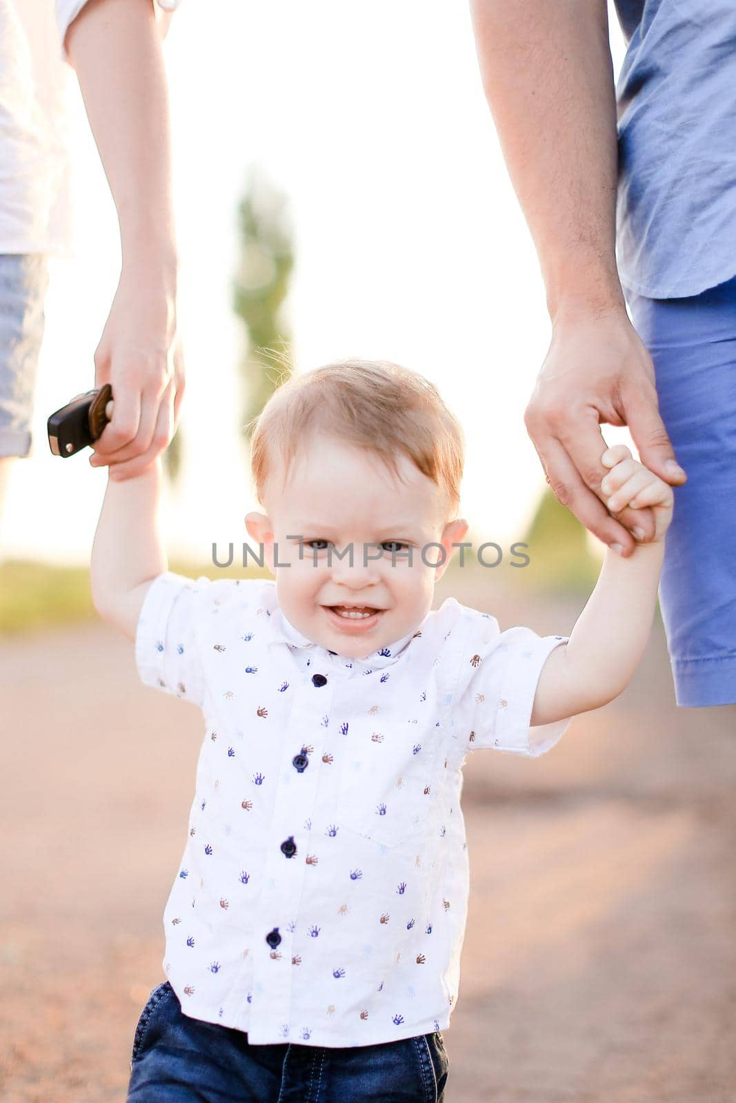 Little smiling child holding parents hands and walking on road. Concept of childhood and resting on open air.