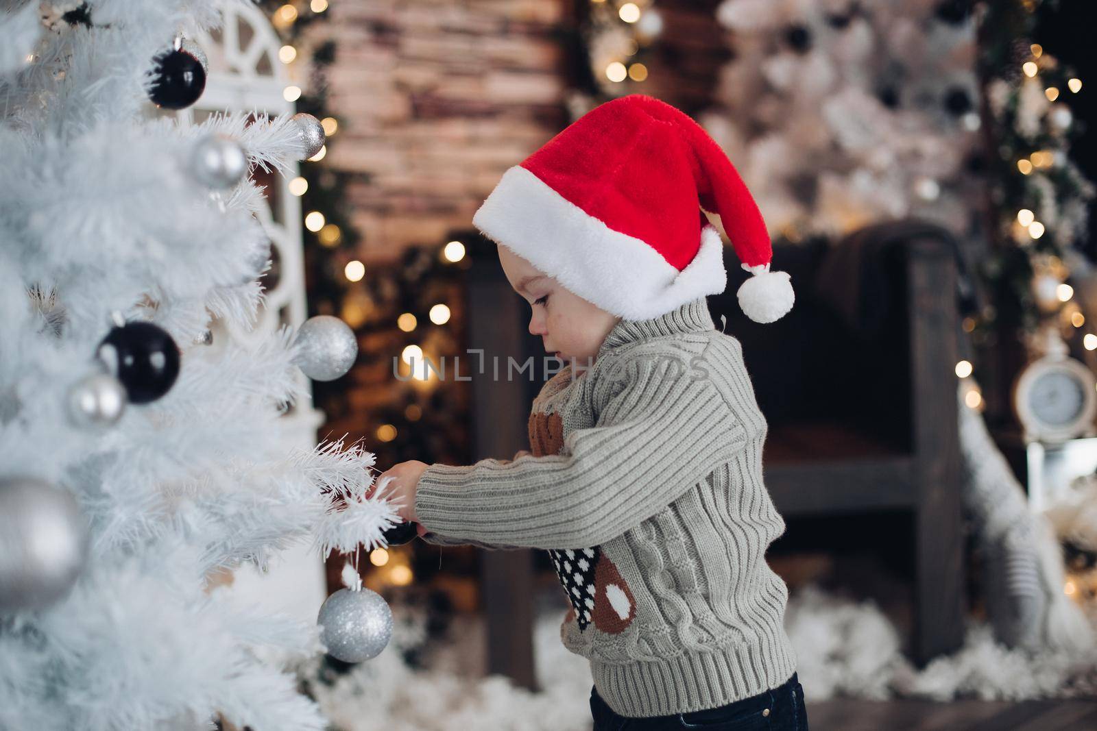 Little cute boy decorates a big New Year's white christmas tree by StudioLucky