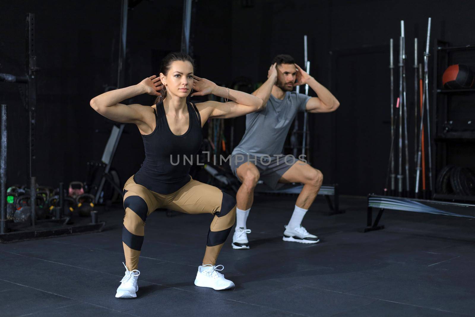 Fitness couple in sportswear doing squat exercises at gym