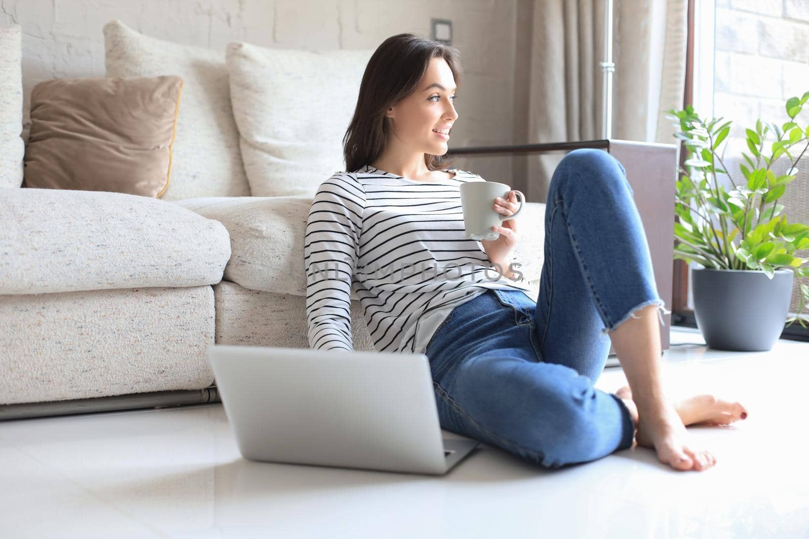 Pretty woman working with laptop while sitting on floor at home and drinking coffee. by tsyhun