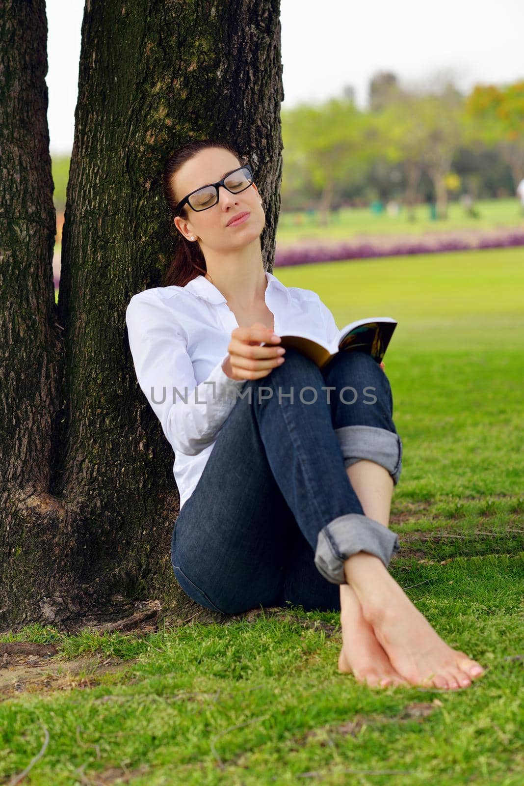 Young woman reading a book in the park by dotshock