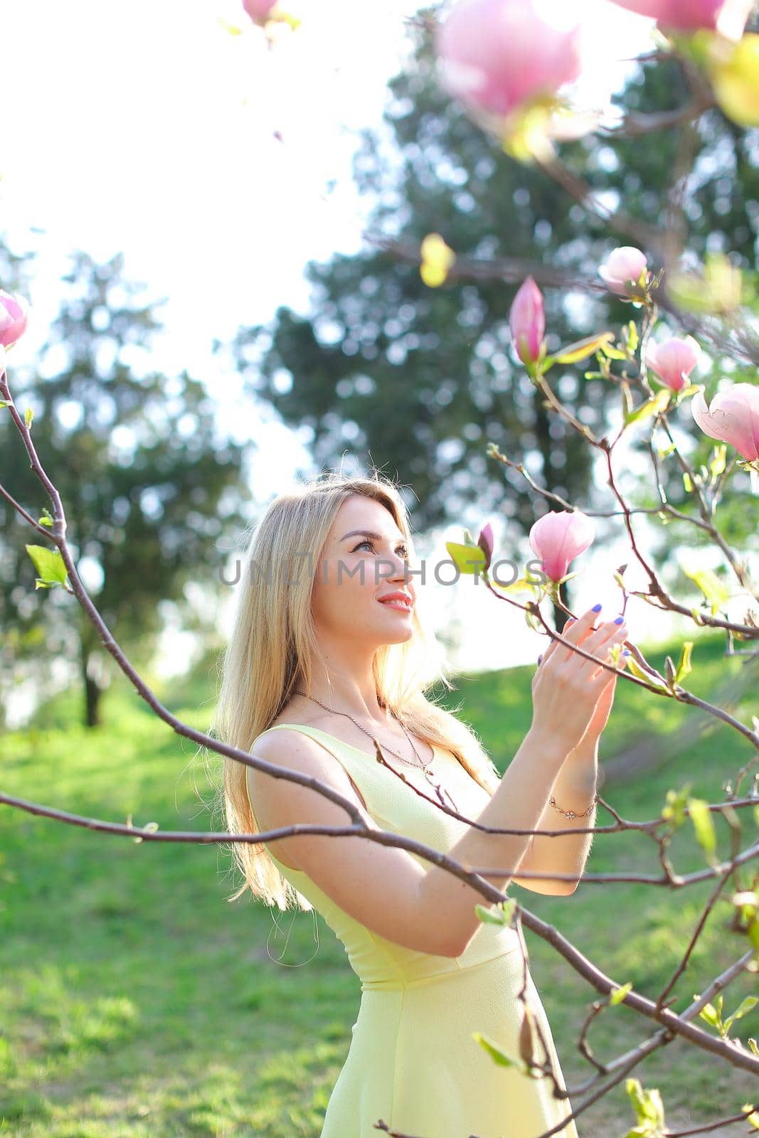 Young blonde girl standing near magnolia in park. Concept of spring seasonal and nature.