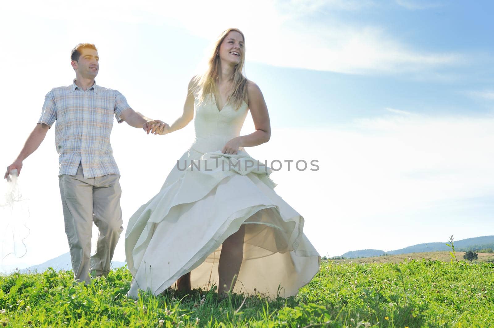 happy bride and groom walking and run on beautiful meadow outdoor at sunset 