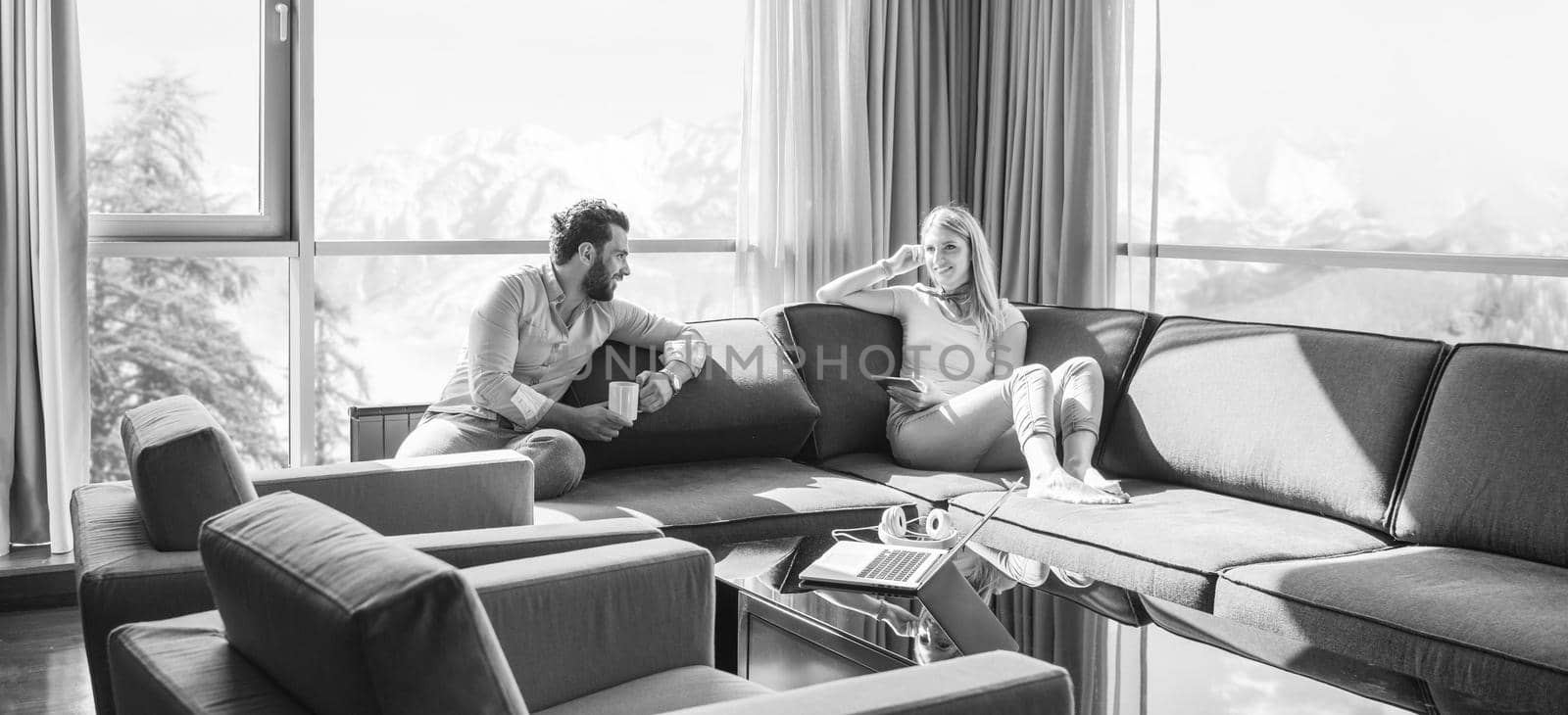 Young couple relaxing at  home using tablet computer reading in the living room near the window on the sofa couch.