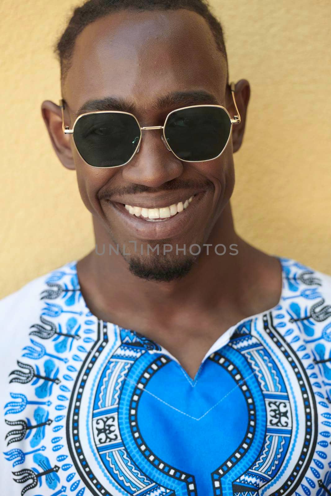 Close up portrait of a smiling young african man wearing traditioinal clothes standing isolated over yellow wall background