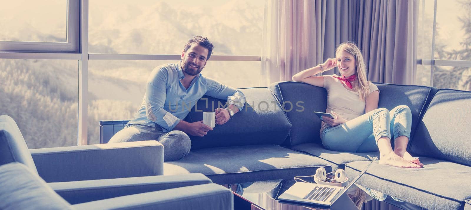 Young couple relaxing at  home using tablet computer reading in the living room near the window on the sofa couch.