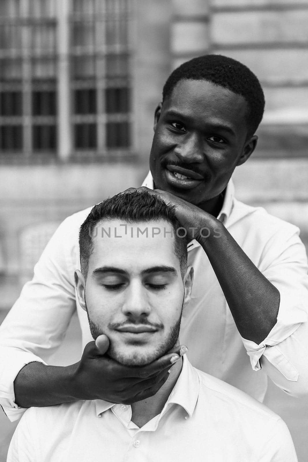 Black and white bw portrait in Paris. Afro american boy holding caucasian guy head by hands, wearing white shirt. Concept of stylish boy and haircut.