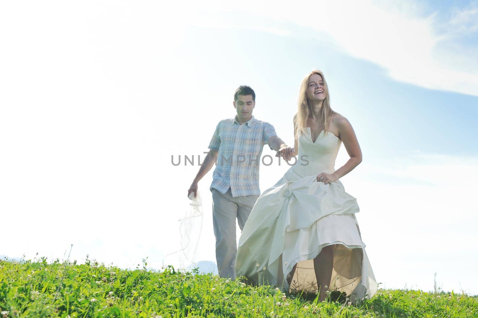 happy bride and groom walking and run on beautiful meadow outdoor at sunset 