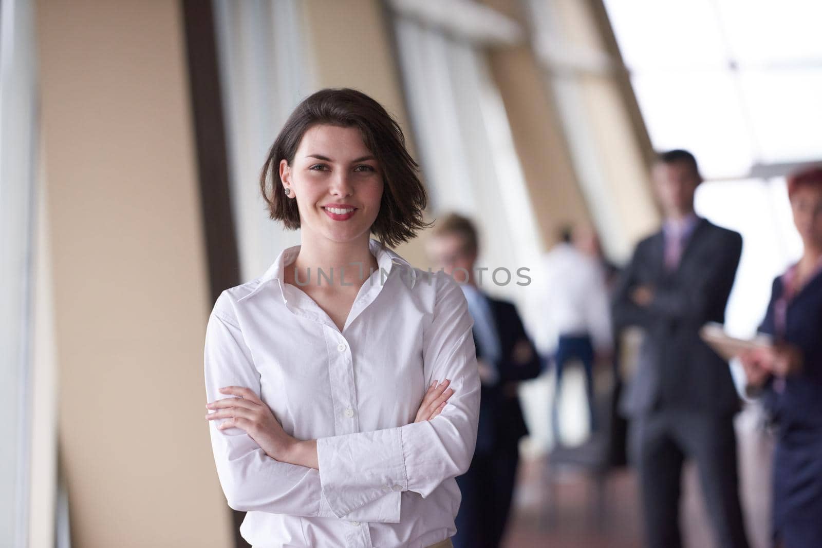 Smilling young business woman in front her team blured in background. Group of young business people. Modern bright  startup office interior.