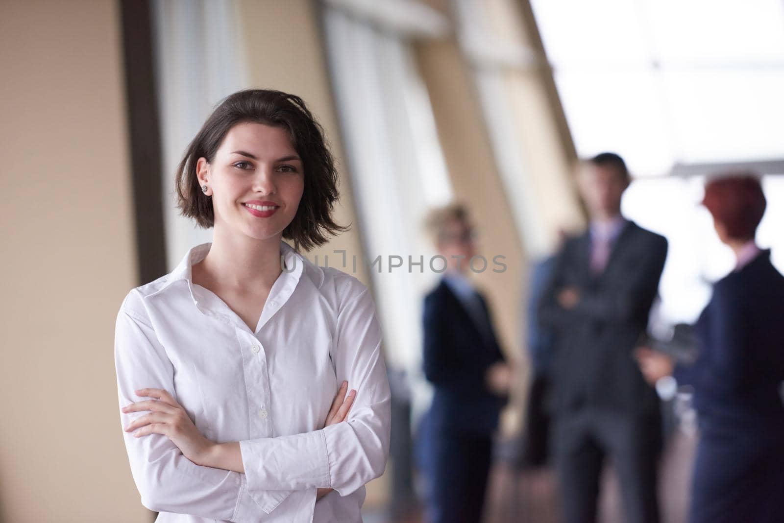 Smilling young business woman in front her team blured in background. Group of young business people. Modern bright  startup office interior.