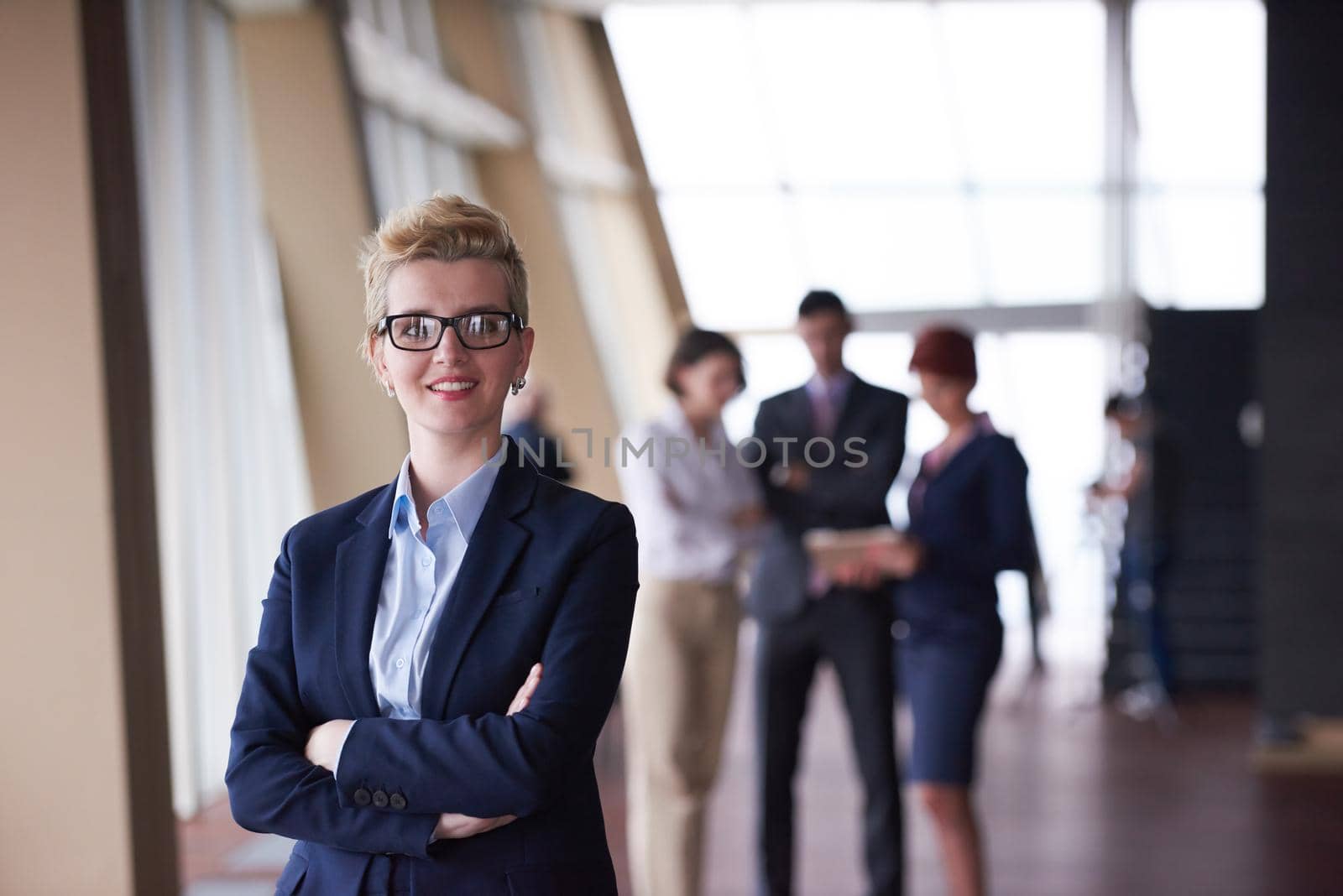 Smilling young business woman in front her team blured in background. Group of young business people. Modern bright  startup office interior.