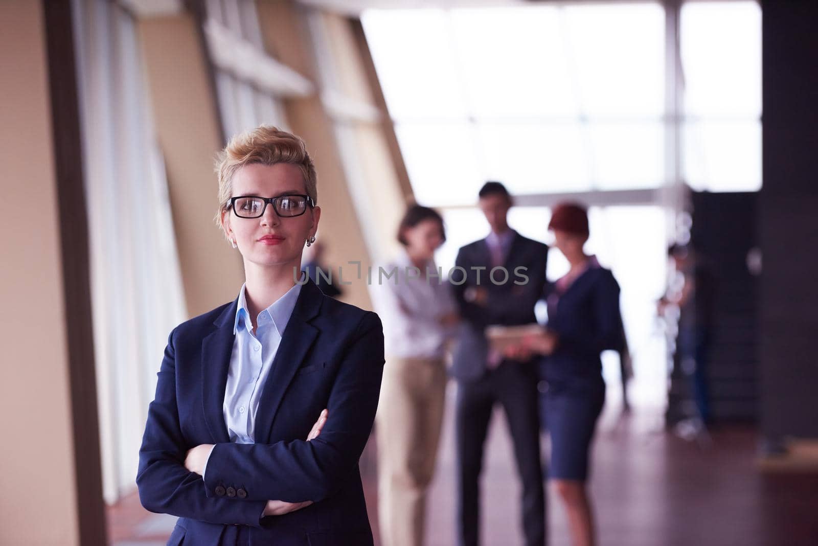 Smilling young business woman in front her team blured in background. Group of young business people. Modern bright  startup office interior.