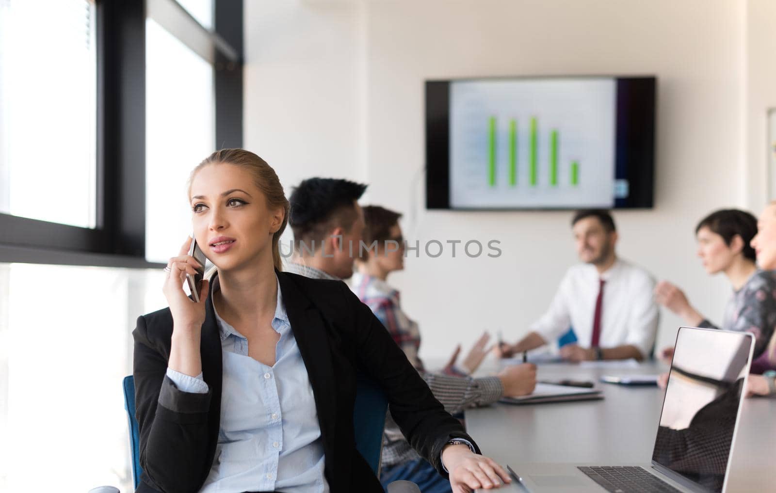 young business woman speaking on phone at modern startup office interior, team in meeting group in background