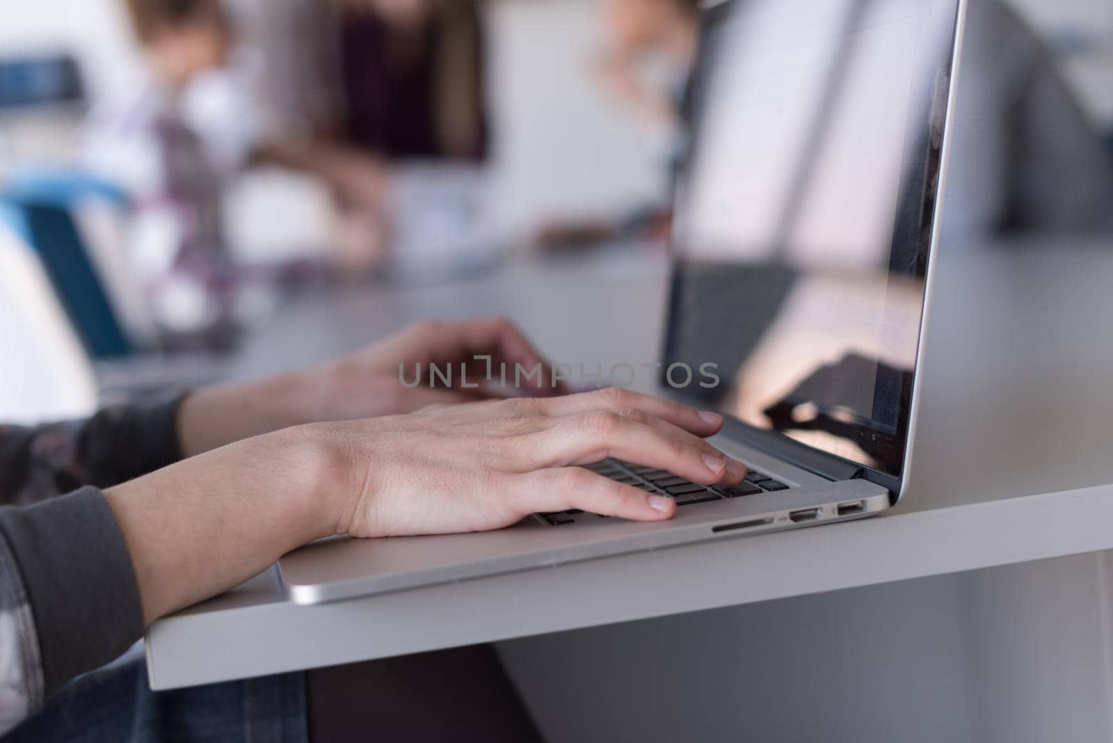 close up of business womans hand typing on laptop with team on meeting in background by dotshock