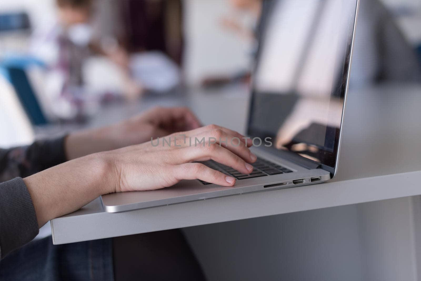 close up of business womans hand typing on laptop with team on meeting in background by dotshock