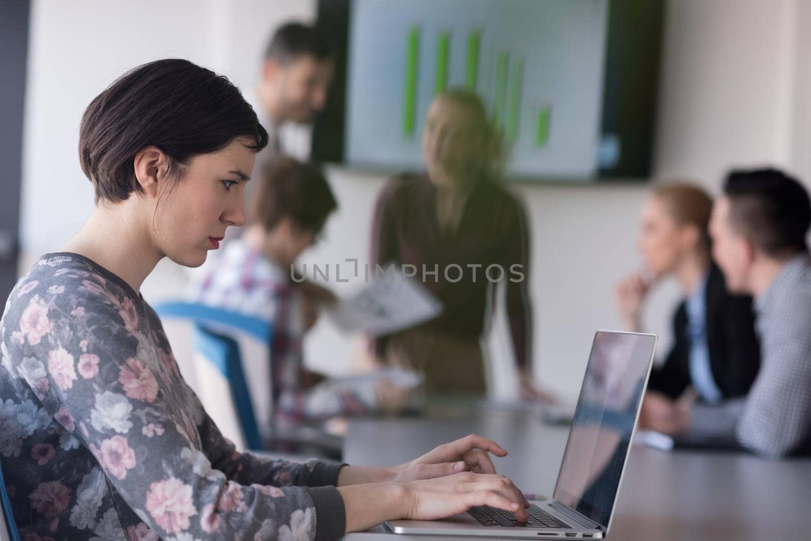 young business woman at office working on laptop with team on meeting in background by dotshock